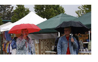Book sale volunteers covered and uncovered the book stalls repeatedly .       Gail Koher and Linda Walker stroll under umbrellas.