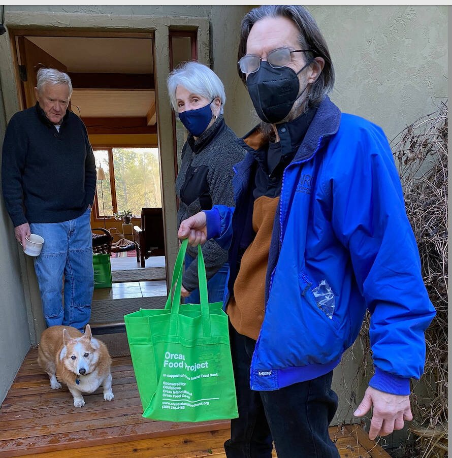 Contributed photo
Victorian Valley Neighborhood Coordinator David Densmore picks up an Orcas Food Project bag from donors Kyla (who goes by one name) and Cy Frazer. Benny, the dog, would like you to know that the Food Bank also provides food for dogs and cats.