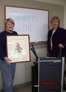 Jane Heisinger with a painting and Michele Streich with a table saw that will be for sale at Granny's Attic on April 18.
