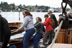 Passengers haul in unison to lift the sails.