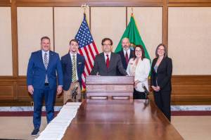 Rick Hughes (back right) with Washington State Gov. Bob Ferguson at the podium.